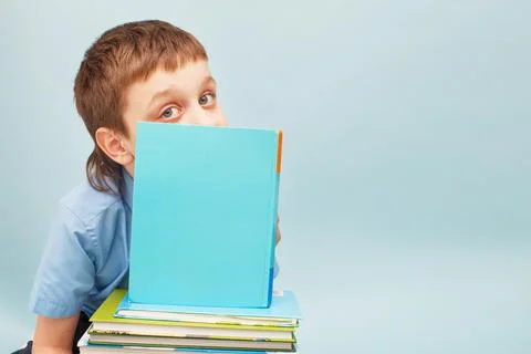 Schoolboy is sitting with a stack of books and reading and covers his face wi Foto stock