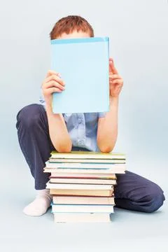 Schoolboy is sitting with a stack of books and reading and covers his face wi Fotos Stock