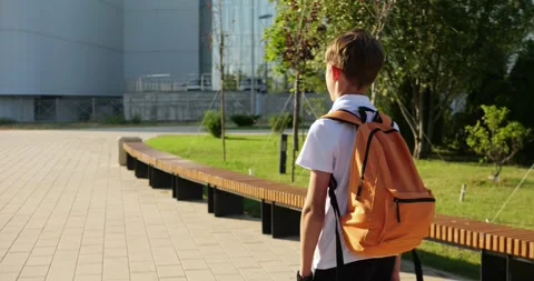 Schoolboy student with orange backpack is walking across modern school campus Stock Footage 346690903