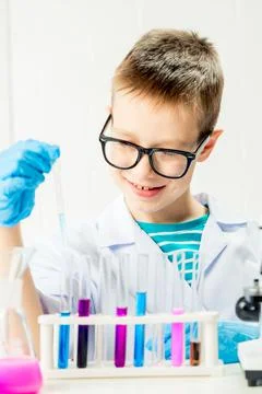 A schoolboy studies multi-colored substances in test tubes, conducts experime Stock Photos