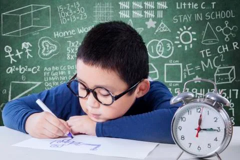 Schoolboy studying with a clock on the table Stock Photos