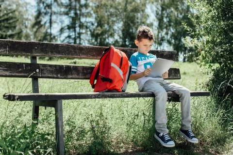Schoolboy taking a break playing with a tablet on a bench Stock Photos