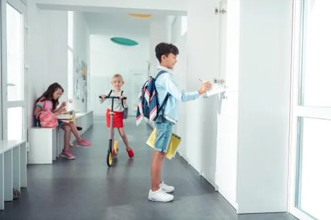 Schoolboy taking notebook from locker standing in the school corridor Foto stock
