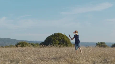 Schoolboy throwing paper plane in field on summer day Stock Footage 129423225
