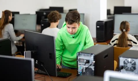 Schoolboy using computer at lesson, teacher teaching pupils in class room Foto stock