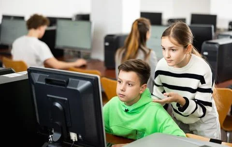 Schoolboy using computer at lesson, teacher teaching pupils in class room Stockfoto's