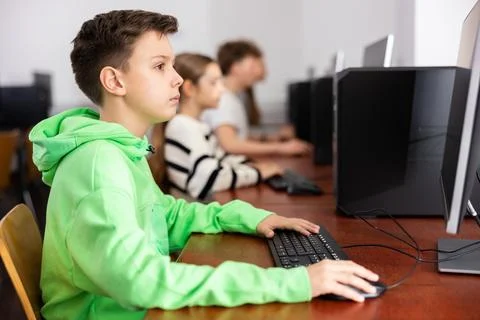 Schoolboy using computer at lesson, teacher teaching pupils in class room Stockfoto's