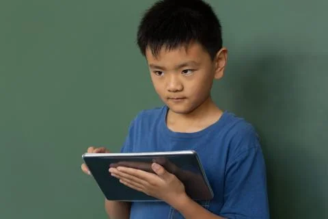 Schoolboy using digital table against greenboard in a classroom Stock Photos