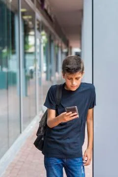 Schoolboy using smart phone while standing by column against building Fotos de archivo