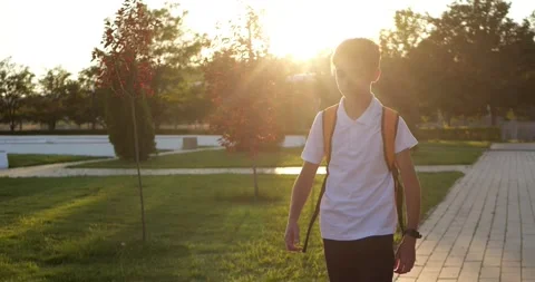 Schoolboy walks through park with backpack. Young student adjusts shoulder Stock Footage 345475517