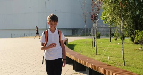Schoolboy walks through school campus with backpack. Teen student checks Stock Footage 344522558