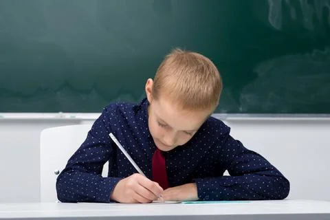 Schoolboy writes in a notebook sitting at a desk Stock Photos