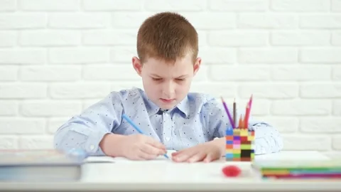 Schoolboy writes in a notebook sitting at a white table. Stock-Footage 151382387