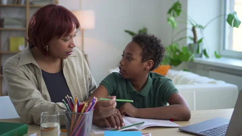 Schoolboy writing in notebook and talking with mother while sitting at table in Stock Footage 163818917