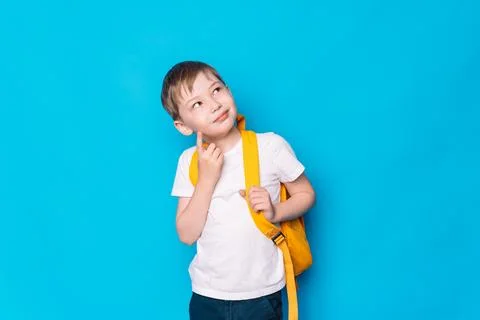Schoolboy with a yellow backpack thought against a blue background Foto stock