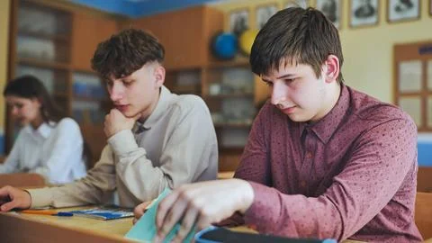 Schoolboys at a desk during class. The boy eats an apple. Stock Photos