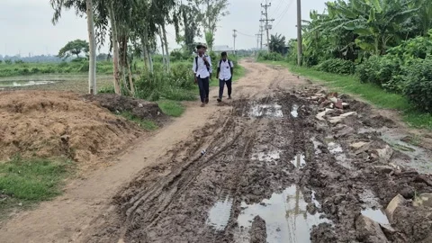 Schoolboys Walking Along Edge Of Muddy Potholed Rural Road Stock Footage 337389598