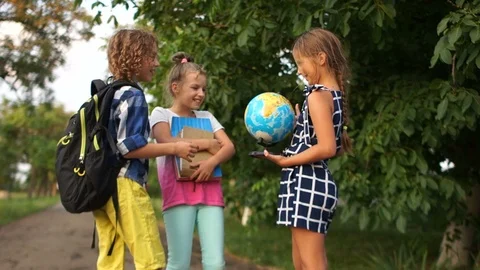 Schoolchildren consider a large globe standing on the street after school Stock Footage 114109163