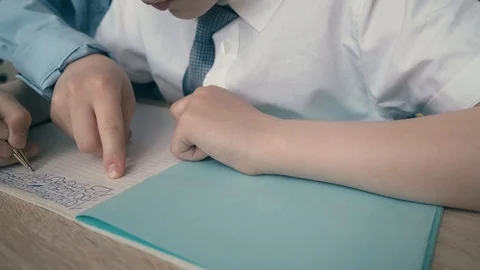Schoolchildren do homework, write numbers in notebook, helping each other. Stock Footage 105098596