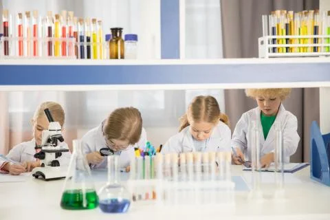 Schoolchildren in lab coats studying together in chemical laboratory Stock Photos