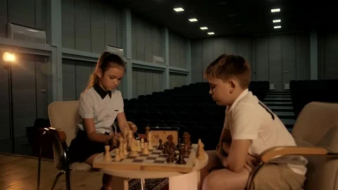 Schoolchildren sit in the hall at a table and focus on a game of chess. Stock Footage 156700495