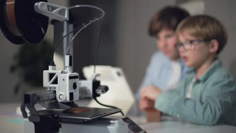 Schoolchildren at a table with a working 3D printer, observing and operating it Stock Footage 335376828
