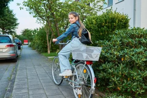 Schoolgirl child 10, 11 years old with backpack on bicycle on street near house Stock Photos
