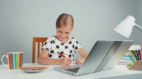 Schoolgirl eating wafer and something writing in her notebook sitting at desk Stock Footage