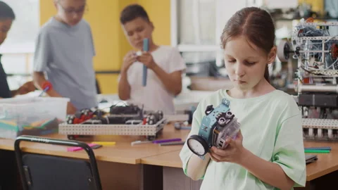 Schoolgirl exploring the assembled moving robot in a class at a robotics lesson Stock Footage 243831486