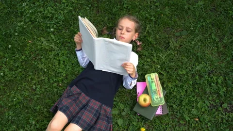Schoolgirl reading book while lying on grass Stock Footage 201229671