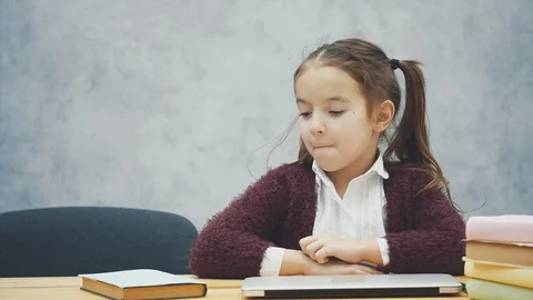 A schoolgirl is sitting at the table. During this time, chooses a book or a Stock Footage 116150992