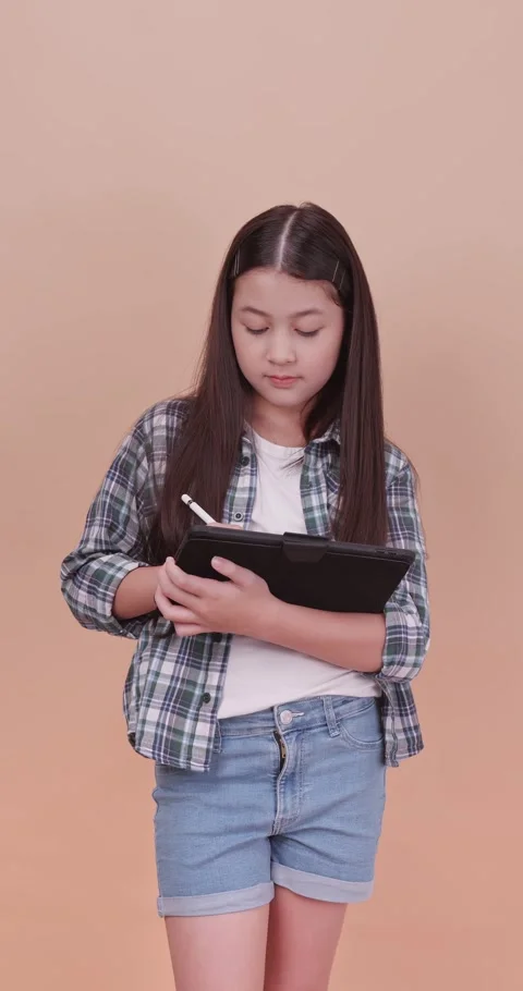 Schoolgirl using computer tablet to study and take notes on brown background. Video stock 253702720