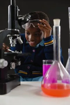 Schoolgirl using microscope against black background Stock Photos