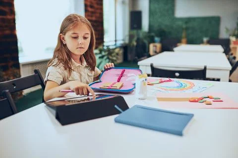 Schoolgirl using tablet. Child doing homework sitting at desk in afterschoo.. Stock Photos