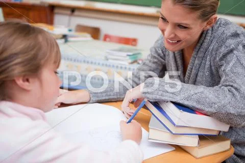 Schoolgirl writing with her smiling teacher Stock Photos