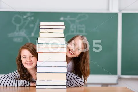 Schoolgirls peeking behind a pile of books Stock Photos