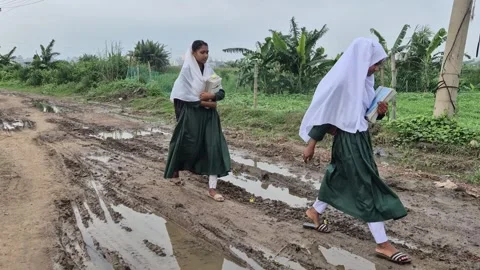 Schoolgirls Walking To School On Muddy Potholed Rural Road Stock Footage 337389645