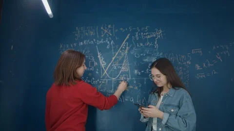 Schoolgirls write on the Board of formulas, talking, looking at the phone Stock Footage 116736323