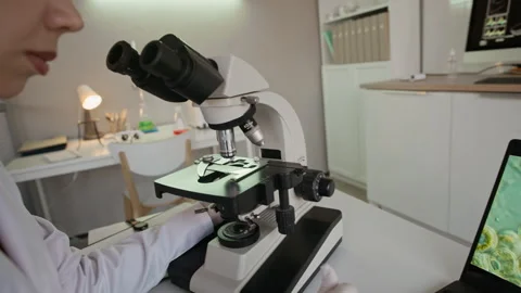 Scientist Analyzing Sample in Microscope and Using Laptop with Molecular System Stock Footage 332360631