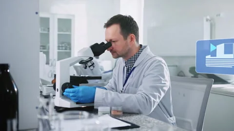 A scientist analyzing samples under a microscope in a fully equipped laboratory Stock Footage 316813186