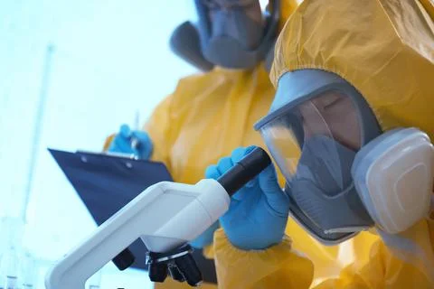 Scientist in chemical protective suit using microscope at laboratory, closeup Stock Photos