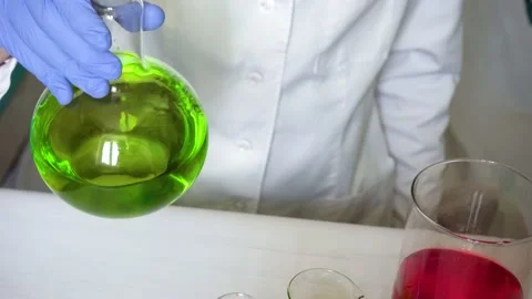 Scientist chemist in blue gloves, white uniform swirls green fluid in glass Stock Footage 222693028