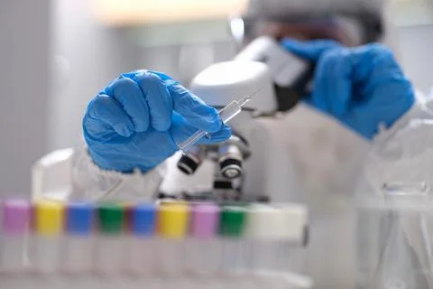Scientist chemist in protective suit looking through microscope in laboratory Stock Photos