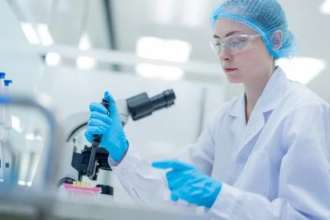 Scientist conducting research in laboratory using pipette and microscope on.. Stock Photos