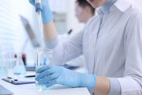 Scientist dripping sample into beaker in laboratory, closeup Foto stock
