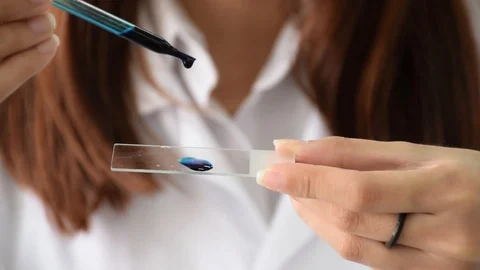 Scientist dropping blue dye on slide with dropper for bacteria testing in lab Stock Footage 87367824