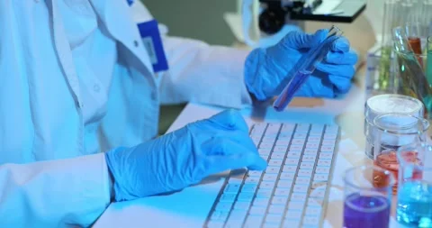 Scientist enters data into computer while holding test tube with blue liquid. Stock Footage 274190629