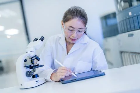 Scientist examines data on tablet while working in laboratory with microsco.. Stock Photos