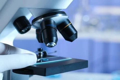 Scientist examining sample of light blue liquid on slide under microscope in  Stock Photos