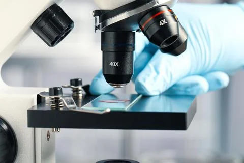 Scientist examining sample of red liquid on slide under microscope in laborat Stock Photos